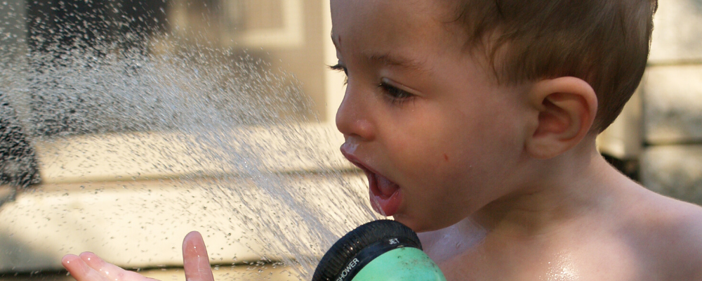 Young boy drinking from hose