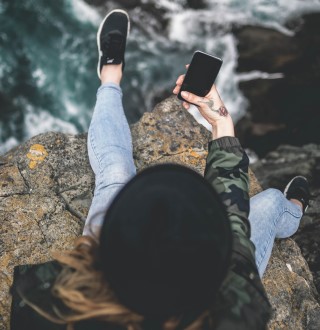 Young woman sitting on cliff with phone